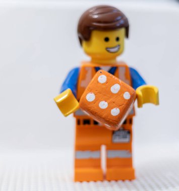 LEGO çalışanı, yüzünde neşeli bir ifadeyle, bir zar Lego Filmi 2 Emmet 'i tutuyor.