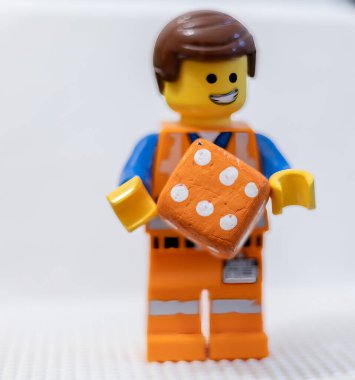 LEGO çalışanı, yüzünde neşeli bir ifadeyle, bir zar Lego Filmi 2 Emmet 'i tutuyor.