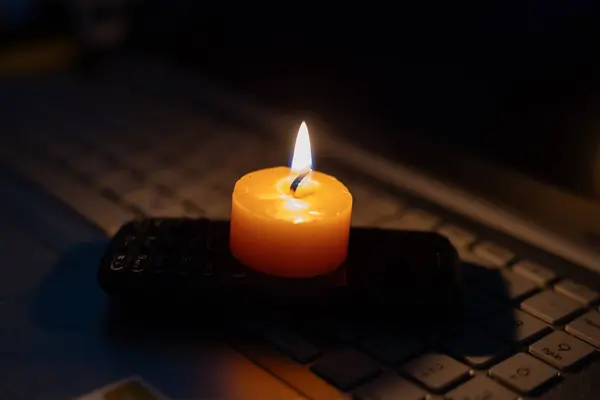 stock image Burning candle on mobile phone and laptop keyboard. No electricity due to war in Ukraine