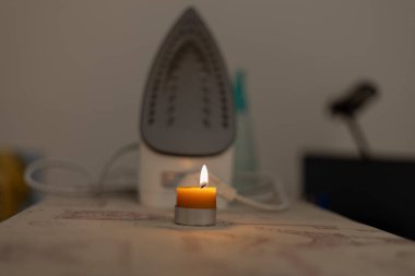 Ütü masasında yanan bir mum ve ütü. Ukrayna 'daki savaştan dolayı elektrik yok.