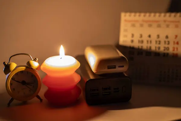 Mekanik saat ve takvimin yanında yanan mum ve güç bankaları. Ukrayna 'daki savaş nedeniyle planlanmış elektrik kesintisi