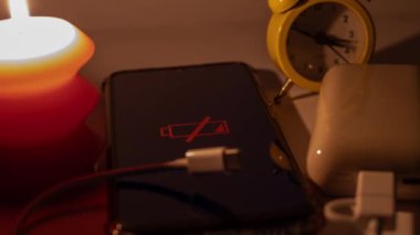 Yanan bir mum ve elektrik bankasının yanında boşaltılmış bir cep telefonu ve mekanik bir saat. Ukrayna 'daki savaş nedeniyle planlanmış elektrik kesintileri