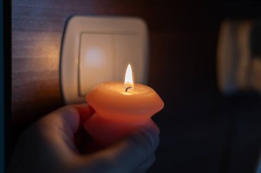 Karanlıkta elinde yanan mum, ışık düğmesinin yanında. Ukrayna 'da savaş nedeniyle elektrik kesintisi