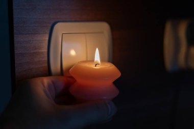 Karanlıkta elinde yanan mum, ışık düğmesinin yanında. Ukrayna 'da savaş nedeniyle elektrik kesintisi