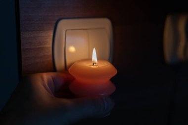 Karanlıkta elinde yanan mum, ışık düğmesinin yanında. Ukrayna 'da savaş nedeniyle elektrik kesintisi