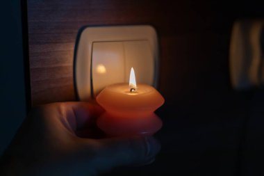 Karanlıkta elinde yanan mum, ışık düğmesinin yanında. Ukrayna 'da savaş nedeniyle elektrik kesintisi