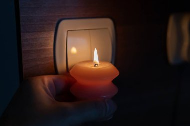 Karanlıkta elinde yanan mum, ışık düğmesinin yanında. Ukrayna 'da savaş nedeniyle elektrik kesintisi