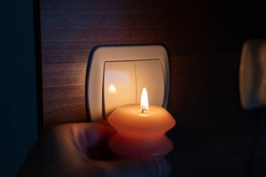 Karanlıkta elinde yanan mum, ışık düğmesinin yanında. Ukrayna 'da savaş nedeniyle elektrik kesintisi