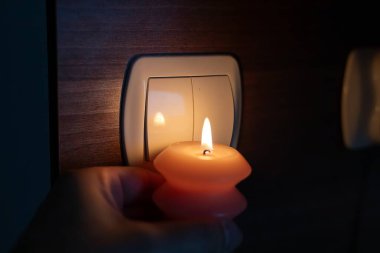 Karanlıkta elinde yanan mum, ışık düğmesinin yanında. Ukrayna 'da savaş nedeniyle elektrik kesintisi