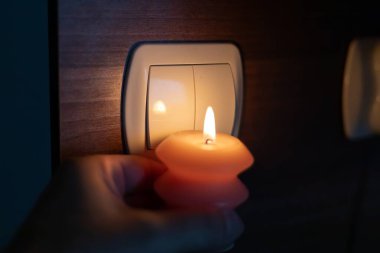 Karanlıkta elinde yanan mum, ışık düğmesinin yanında. Ukrayna 'da savaş nedeniyle elektrik kesintisi
