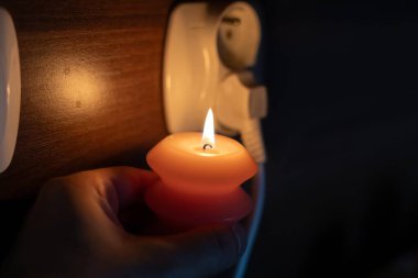 Elinde yanan mum, karanlıkta soketin yanında. Ukrayna 'da savaş nedeniyle elektrik kesintisi