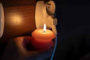 Elinde yanan mum, karanlıkta soketin yanında. Ukrayna 'da savaş nedeniyle elektrik kesintisi