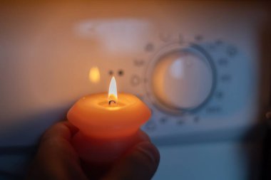 Burning candle in hand near washing machine in the dark. Power outage due to war in Ukraine clipart