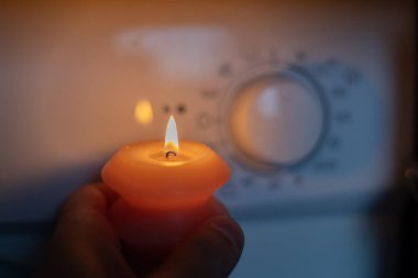Karanlıkta çamaşır makinesinin yanında yanan mum. Ukrayna 'da savaş nedeniyle elektrik kesintisi