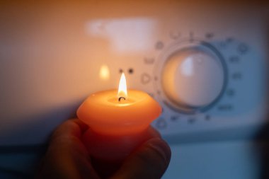 Karanlıkta çamaşır makinesinin yanında yanan mum. Ukrayna 'da savaş nedeniyle elektrik kesintisi
