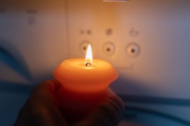 Karanlıkta çamaşır makinesinin yanında yanan mum. Ukrayna 'da savaş nedeniyle elektrik kesintisi