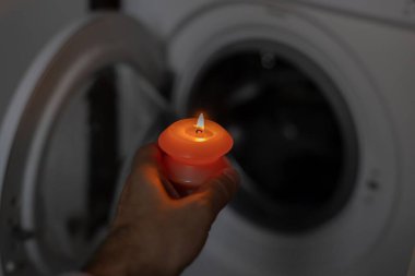 Karanlıkta çamaşır makinesinin yanında yanan mum. Ukrayna 'da savaş nedeniyle elektrik kesintisi