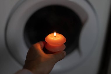 Karanlıkta çamaşır makinesinin yanında yanan mum. Ukrayna 'da savaş nedeniyle elektrik kesintisi