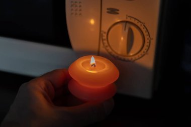 Elinde yanan mum, karanlıkta mikrodalga fırının yanında. Ukrayna 'da savaş nedeniyle elektrik kesintisi