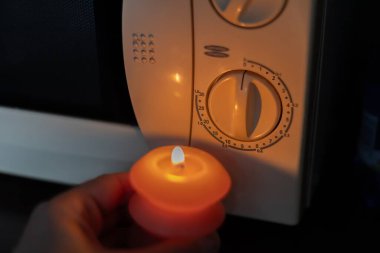 Elinde yanan mum, karanlıkta mikrodalga fırının yanında. Ukrayna 'da savaş nedeniyle elektrik kesintisi