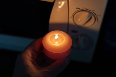 Elinde yanan mum, karanlıkta mikrodalga fırının yanında. Ukrayna 'da savaş nedeniyle elektrik kesintisi