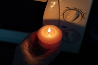 Elinde yanan mum, karanlıkta mikrodalga fırının yanında. Ukrayna 'da savaş nedeniyle elektrik kesintisi
