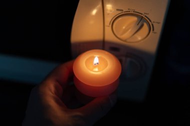 Elinde yanan mum, karanlıkta mikrodalga fırının yanında. Ukrayna 'da savaş nedeniyle elektrik kesintisi
