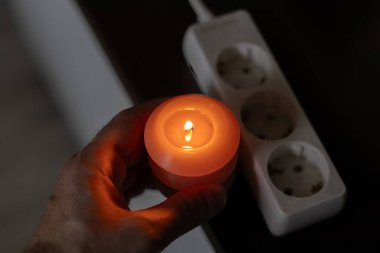 Elinde yanan mum, karanlıkta soketin yanında. Ukrayna 'da savaş nedeniyle elektrik kesintisi