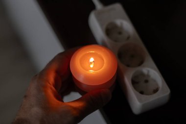 Elinde yanan mum, karanlıkta soketin yanında. Ukrayna 'da savaş nedeniyle elektrik kesintisi