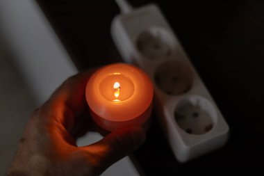 Elinde yanan mum, karanlıkta soketin yanında. Ukrayna 'da savaş nedeniyle elektrik kesintisi