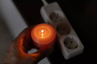 Elinde yanan mum, karanlıkta soketin yanında. Ukrayna 'da savaş nedeniyle elektrik kesintisi