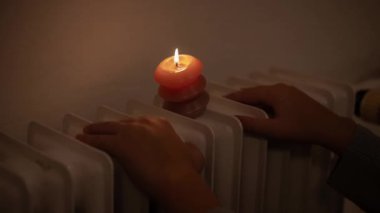 Çocuk elleri ve radyatörde yanan bir mum. Ukrayna 'daki savaş nedeniyle ısıtma ve elektrik sorunları