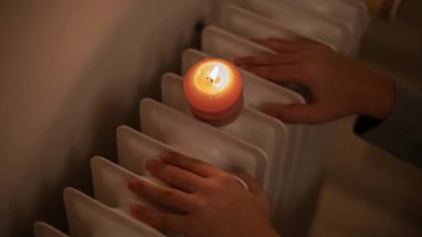 Çocuk elleri ve radyatörde yanan bir mum. Ukrayna 'daki savaş nedeniyle ısıtma ve elektrik sorunları