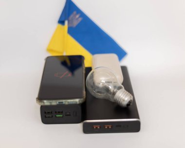 Güç bankaları, boşaltılmış bir telefon ve Ukrayna bayrağına karşı çalışmayan bir ampul. Ukrayna 'daki savaş nedeniyle elektrik kesintileri