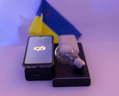 Güç bankaları, boşaltılmış bir telefon ve Ukrayna bayrağına karşı çalışmayan bir ampul. Ukrayna 'daki savaş nedeniyle elektrik kesintileri