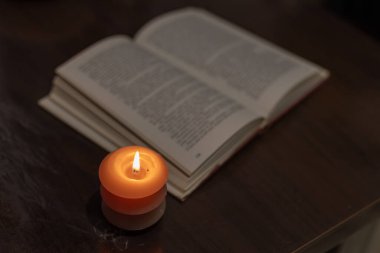 Karanlıkta açık bir kitabın yanında yanan mum. Ukrayna 'da savaş nedeniyle elektrik kesintisi