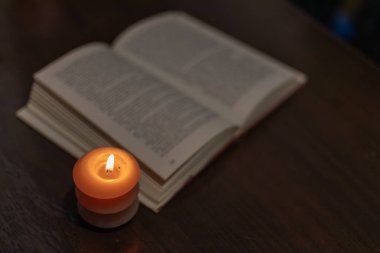 Karanlıkta açık bir kitabın yanında yanan mum. Ukrayna 'da savaş nedeniyle elektrik kesintisi