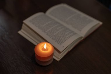 Karanlıkta açık bir kitabın yanında yanan mum. Ukrayna 'da savaş nedeniyle elektrik kesintisi