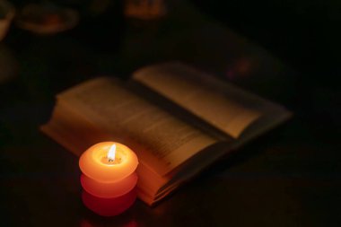 Karanlıkta açık bir kitabın yanında yanan mum. Ukrayna 'da savaş nedeniyle elektrik kesintisi