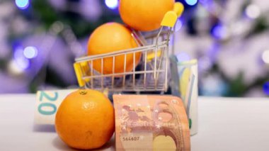 Bir sepetin içinde mandalinalar ve bir Noel ağacının arka planında banknotlar. Tatilden önce artan gıda fiyatları
