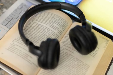 Bilgisayarın yanında açık bir kitaptaki kulaklıklar.