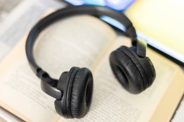 Bilgisayarın yanında açık bir kitaptaki kulaklıklar.