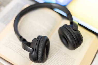 Bilgisayarın yanında açık bir kitaptaki kulaklıklar.