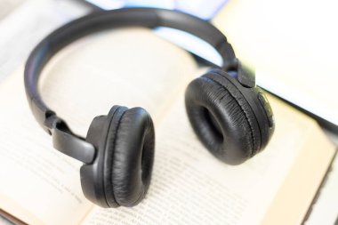 Bilgisayarın yanında açık bir kitaptaki kulaklıklar.