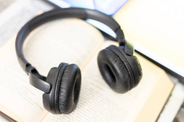 Bilgisayarın yanında açık bir kitaptaki kulaklıklar.