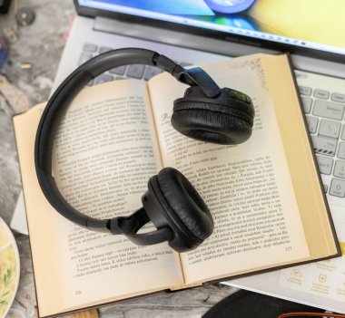 Bilgisayarın yanında açık bir kitaptaki kulaklıklar.