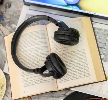 Bilgisayarın yanında açık bir kitaptaki kulaklıklar.