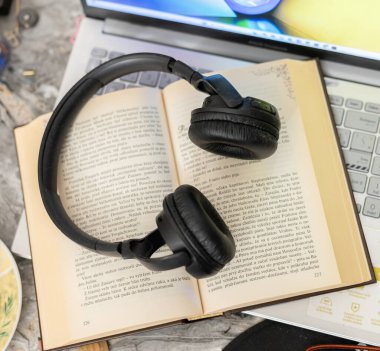 Bilgisayarın yanında açık bir kitaptaki kulaklıklar.