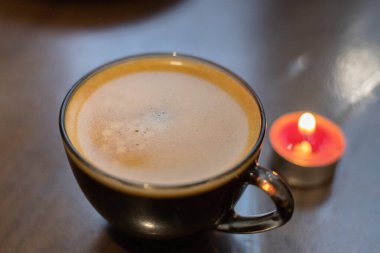 Şeffaf bir fincanda kahve ve yakınlarda yanan bir mum. Elektriksel sorunlar nedeniyle karartma