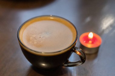 Şeffaf bir fincanda kahve ve yakınlarda yanan bir mum. Elektriksel sorunlar nedeniyle karartma